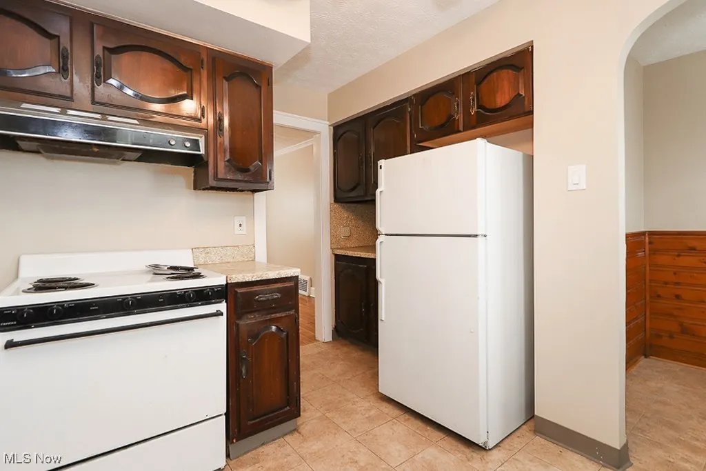 Kitchen featuring white appliances, dark brown cabinets, arched walkways, and under cabinet range hood