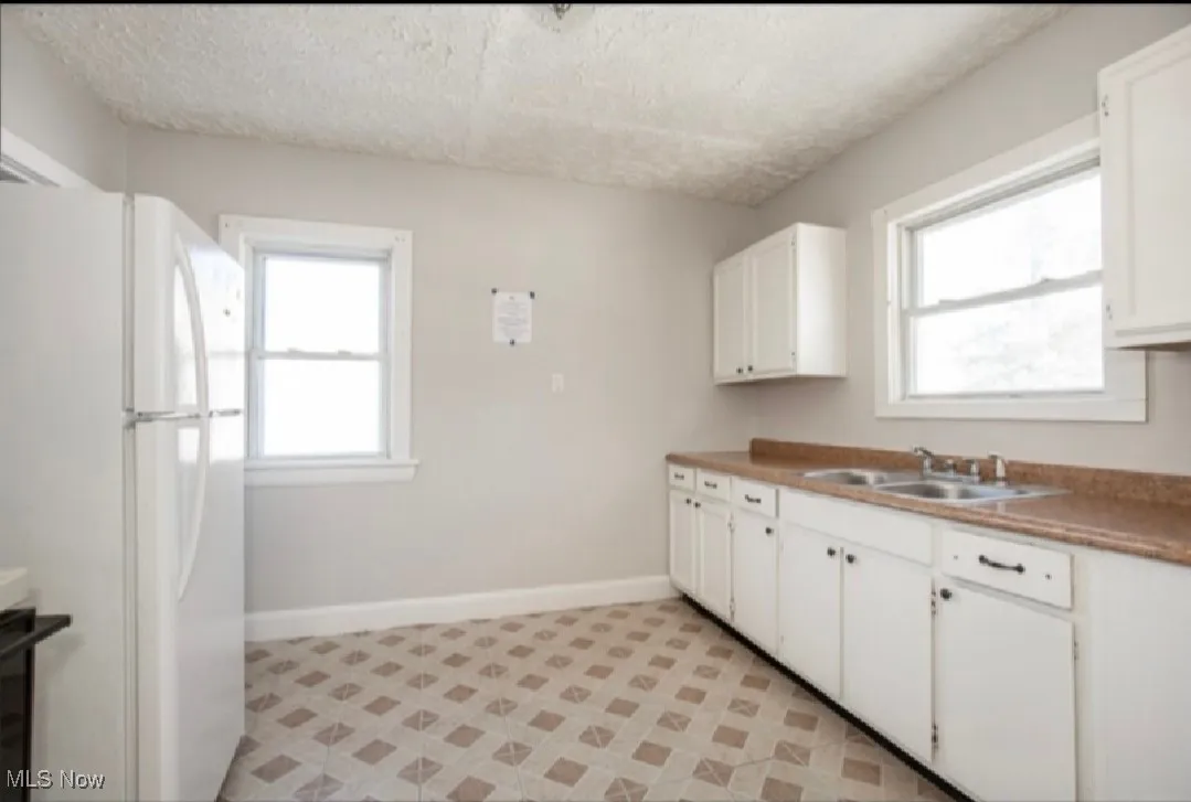 Kitchen with a sink, baseboards, white cabinets, and freestanding refrigerator