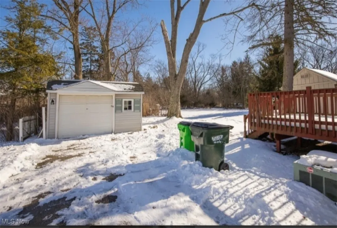 Yard layered in snow featuring a detached garage, an outdoor structure, and a deck