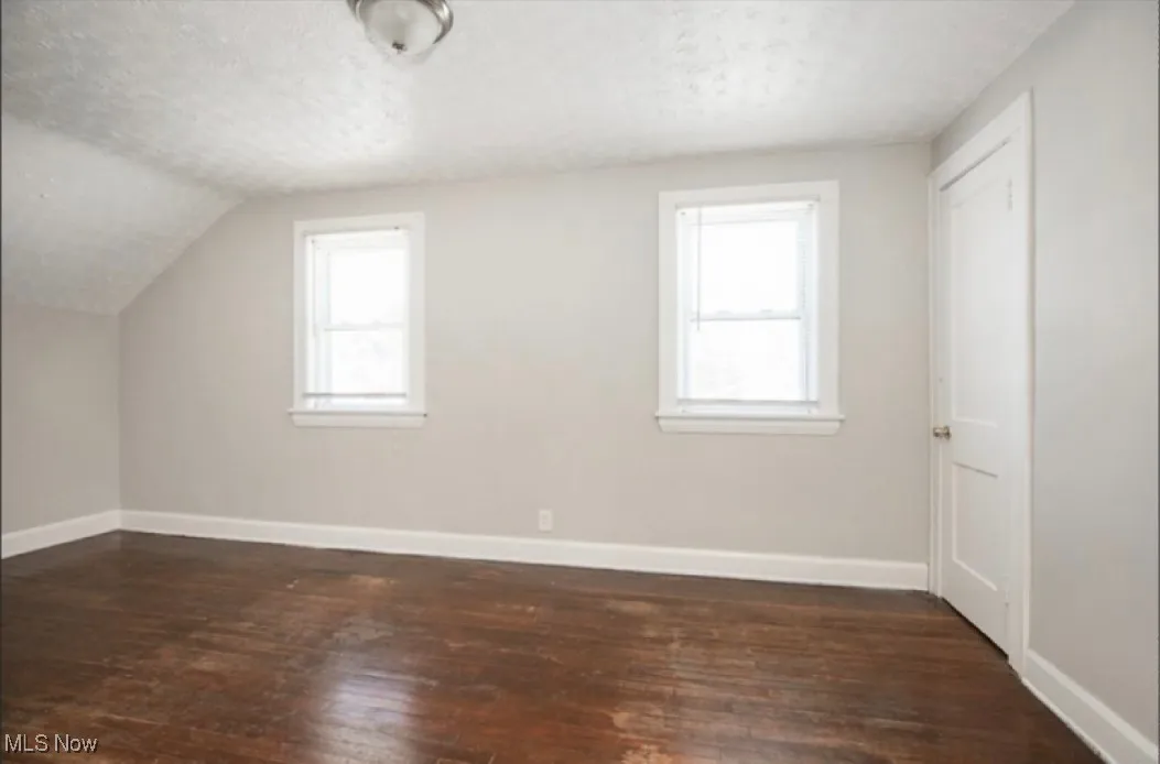 Bonus room featuring a textured ceiling, baseboards, and dark wood-style flooring