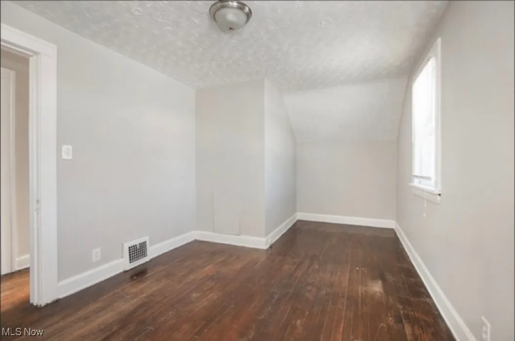 Additional living space with vaulted ceiling, a textured ceiling, baseboards, and wood-type flooring