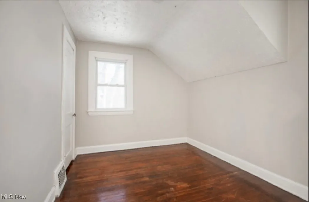 Bonus room with visible vents, baseboards, lofted ceiling, dark wood-style flooring, and a textured ceiling