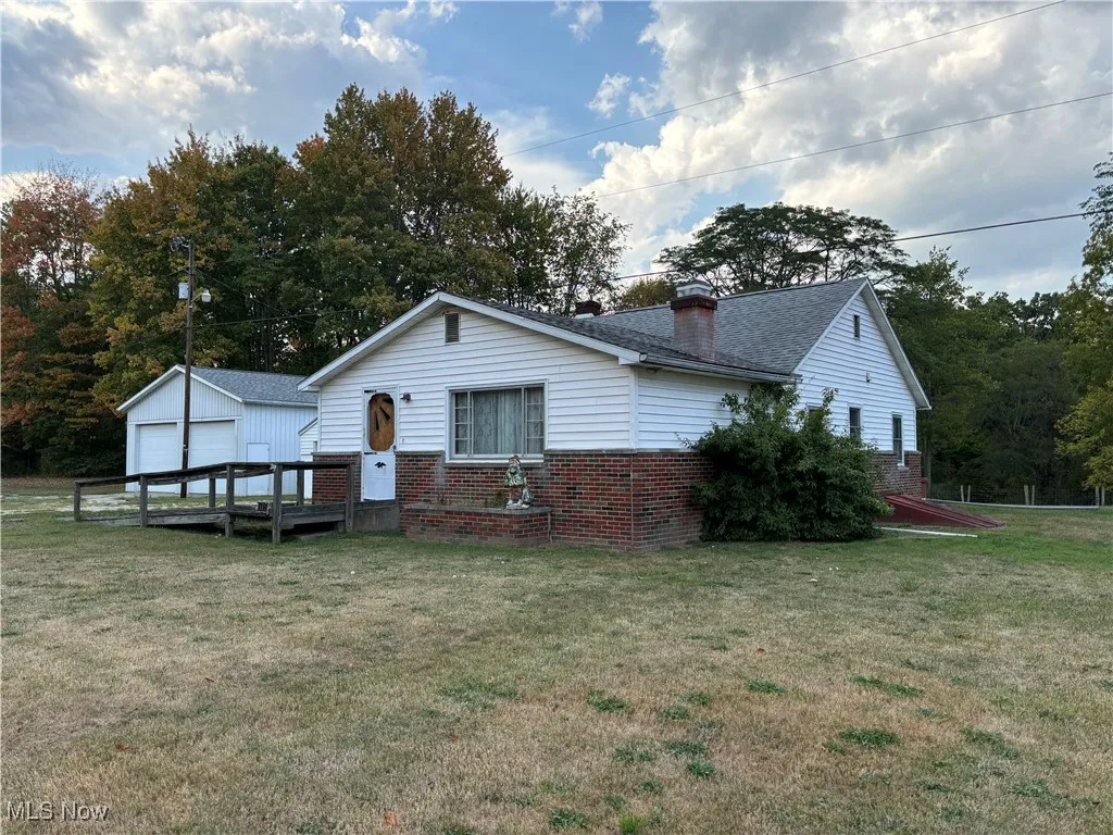 Rear view of property featuring brick siding, a lawn, a chimney, a garage, and an outdoor structure