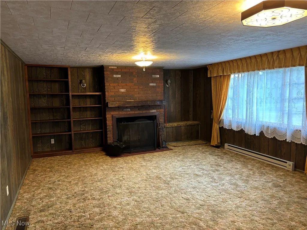 Unfurnished living room with wooden walls, a baseboard heating unit, visible vents, and carpet floors
