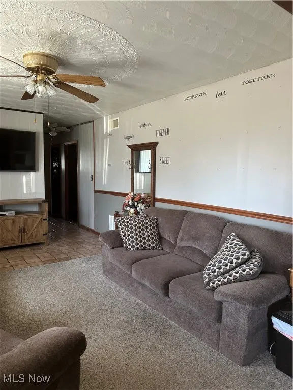 Living room with light colored carpet, visible vents, a ceiling fan, light tile patterned flooring, and a textured ceiling