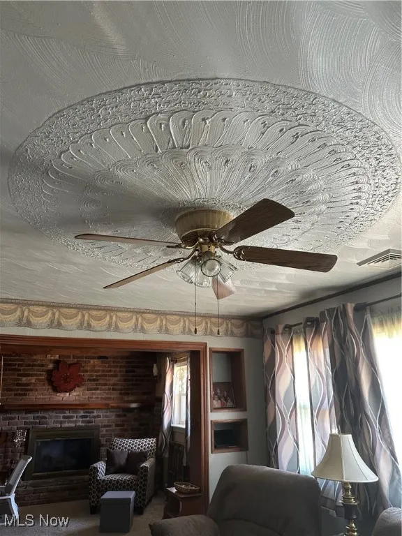 Living room with visible vents, a fireplace, brick wall, and ceiling fan