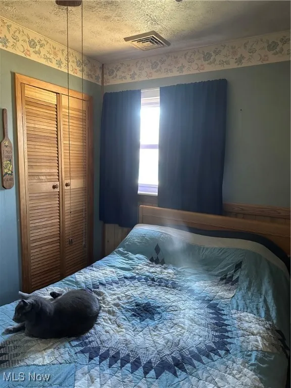 Bedroom with a closet, visible vents, and a textured ceiling