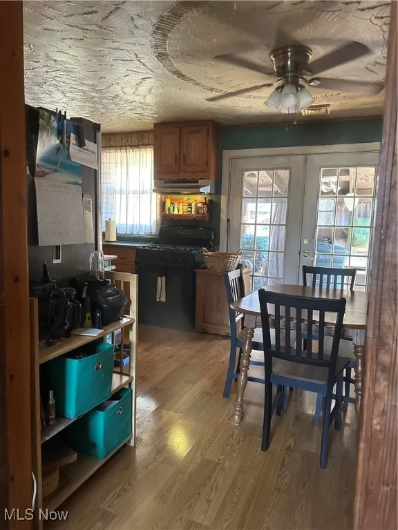 Kitchen with black gas range, light wood finished floors, brown cabinetry, ventilation hood, and french doors