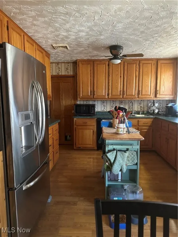 Kitchen featuring refrigerator, brown cabinets, visible vents, a ceiling fan, and wood finished floors