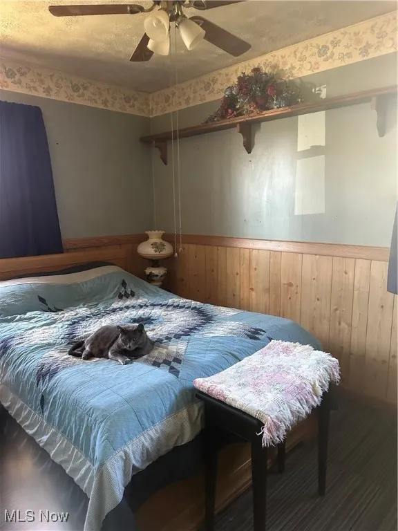 Bedroom with a textured ceiling, ceiling fan, wood walls, and wainscoting