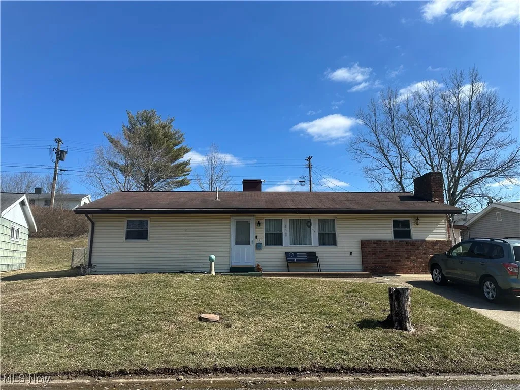 View of front of house with driveway, a chimney, and a front lawn