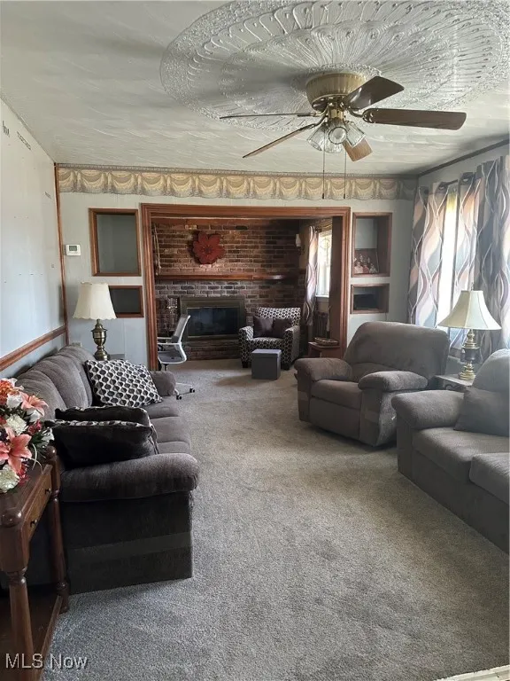 Living room featuring ceiling fan, a brick fireplace, and carpet flooring