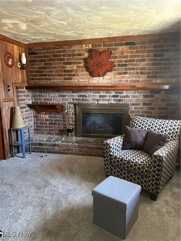 Carpeted living room featuring brick wall, wood walls, and a fireplace