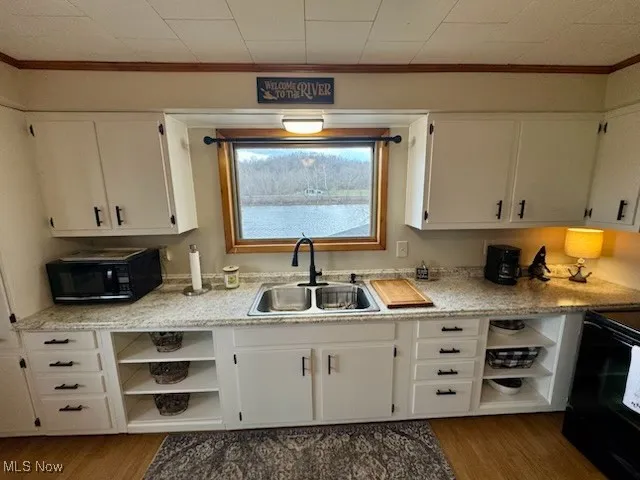 Kitchen with open shelves, white cabinets, black appliances, and a sink