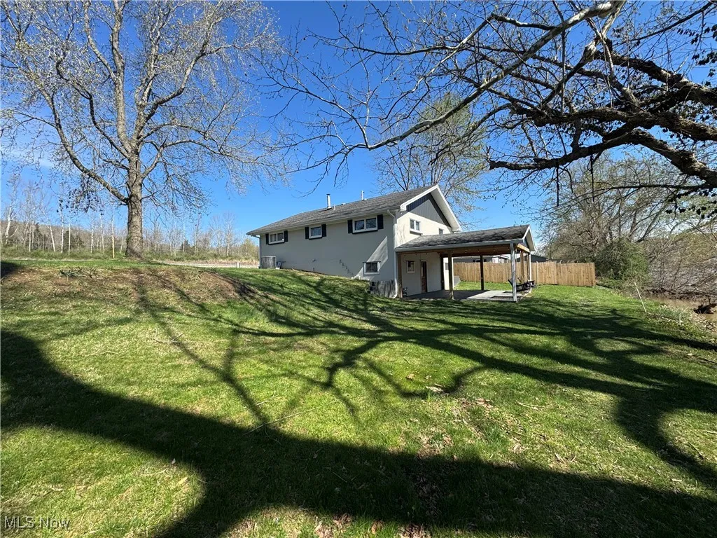 Rear view of house with a carport, fence, a lawn, and stucco siding