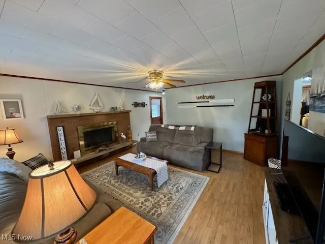Living area with a ceiling fan, wood finished floors, baseboards, a fireplace with raised hearth, and crown molding