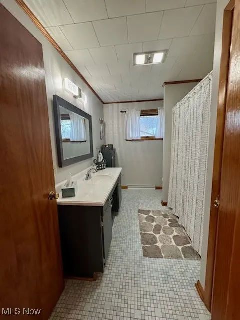 Bathroom featuring a shower with shower curtain, baseboards, vanity, and crown molding