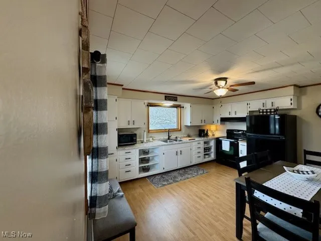 Kitchen featuring a sink, black appliances, white cabinets, light wood-style floors, and crown molding