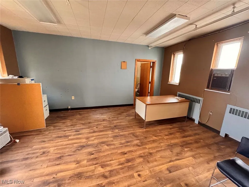 Bedroom with cooling unit, radiator, baseboards, and wood finished floors