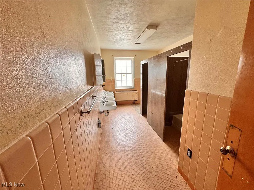 Bathroom with tile walls, radiator heating unit, wainscoting, a textured wall, and a textured ceiling