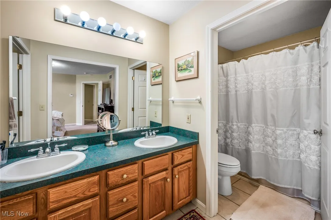 Full bathroom with double vanity, a sink, toilet, and tile patterned flooring