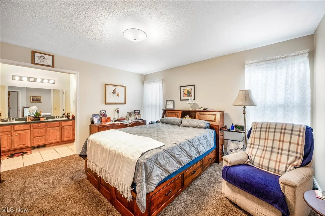Bedroom featuring light colored carpet, light tile patterned floors, a textured ceiling, a sink, and connected bathroom
