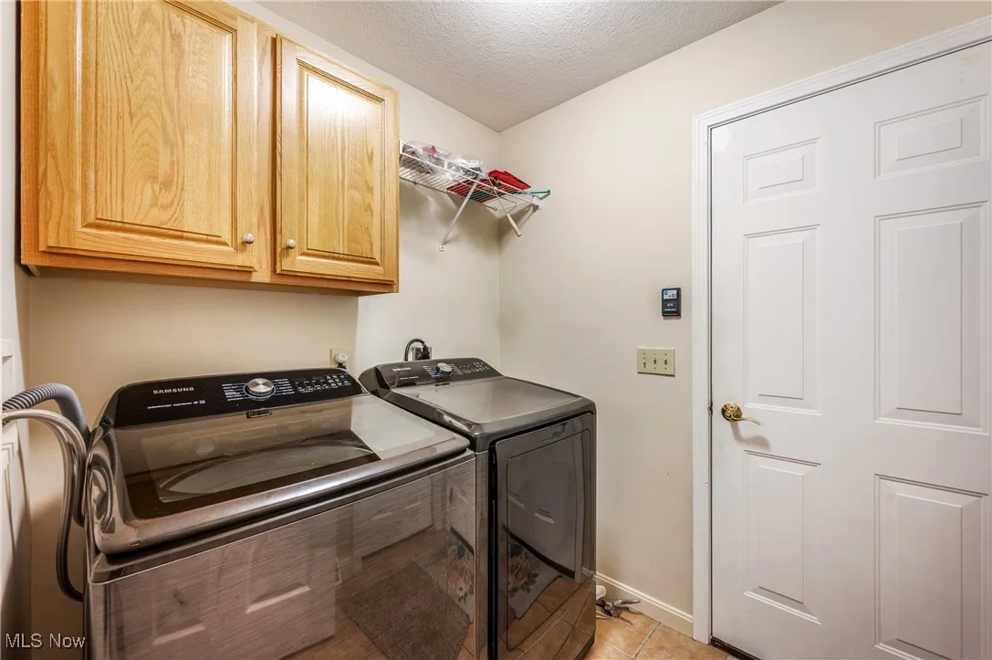 Washroom with light tile patterned flooring, washing machine and clothes dryer, a textured ceiling, baseboards, and cabinet space