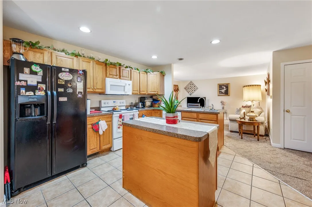 Kitchen featuring white appliances, light carpet, open floor plan, a center island, and light tile patterned floors