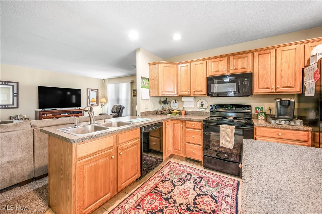 Kitchen with light tile patterned flooring, a peninsula, a sink, open floor plan, and black appliances