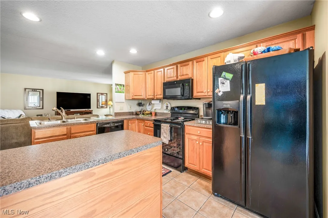 Kitchen with a sink, open floor plan, light tile patterned floors, black appliances, and recessed lighting