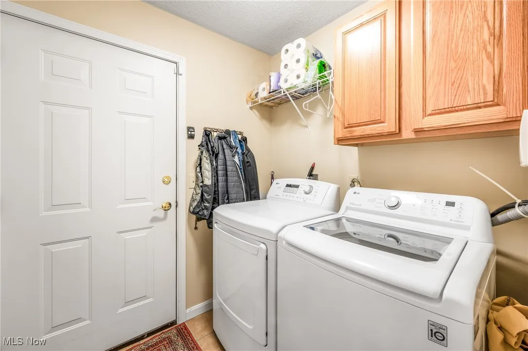 Clothes washing area featuring light tile patterned flooring, cabinet space, a textured ceiling, and washer and clothes dryer