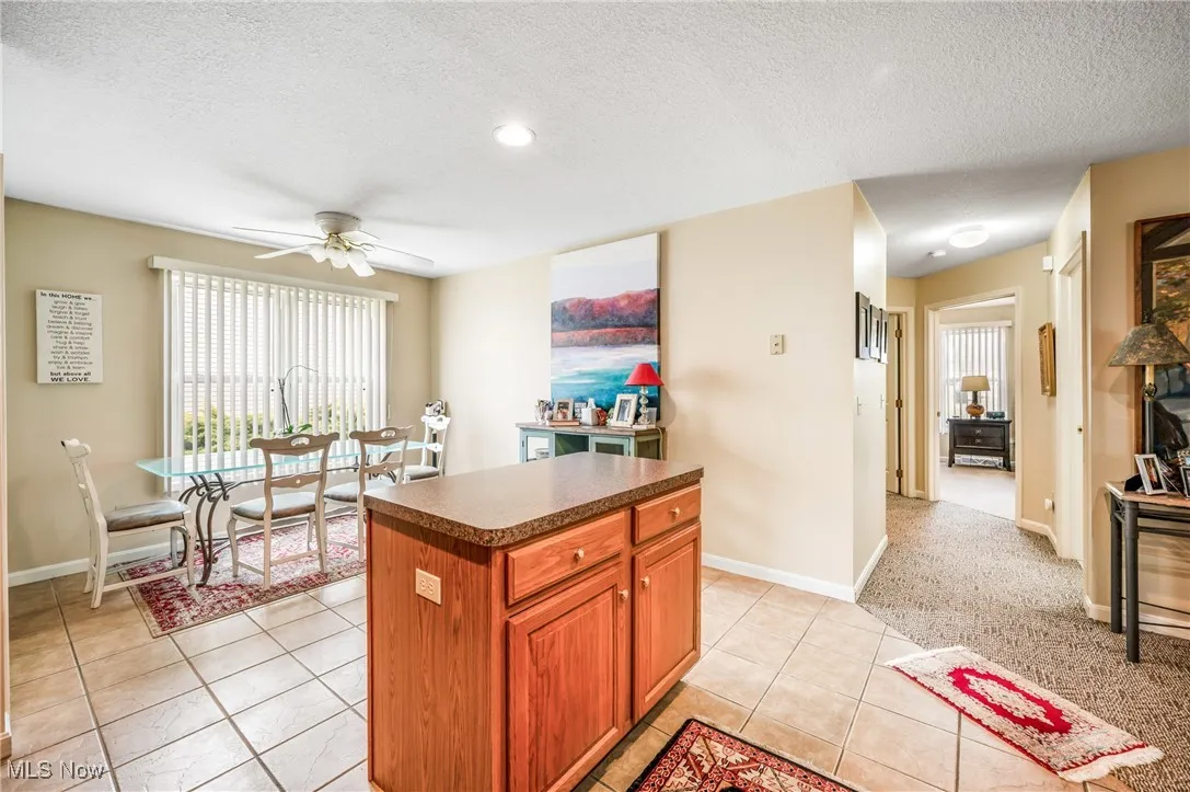 Kitchen featuring a textured ceiling, dark countertops, a ceiling fan, a center island, and light tile patterned floors