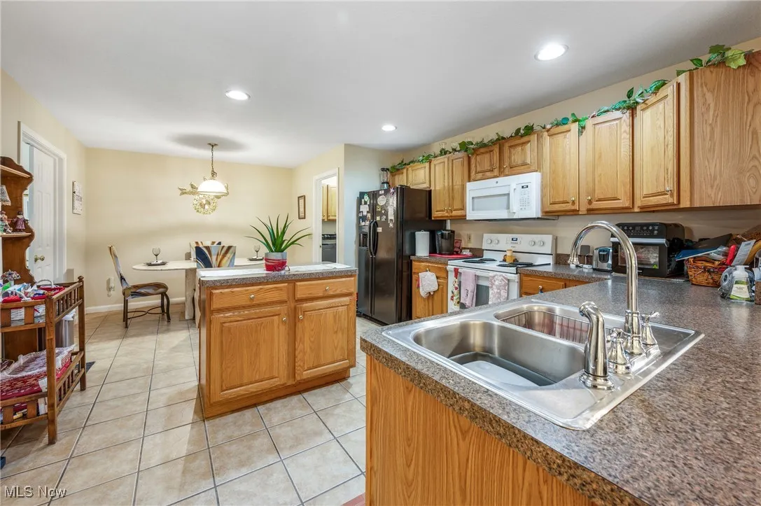 Kitchen with recessed lighting, white appliances, light tile patterned flooring, dark countertops, and a sink