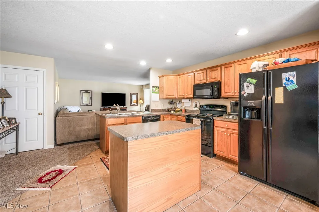 Kitchen featuring a peninsula, black appliances, light tile patterned floors, and open floor plan