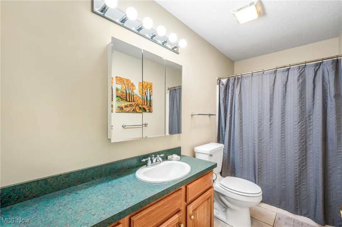Full bathroom with toilet, curtained shower, vanity, tile patterned flooring, and visible vents