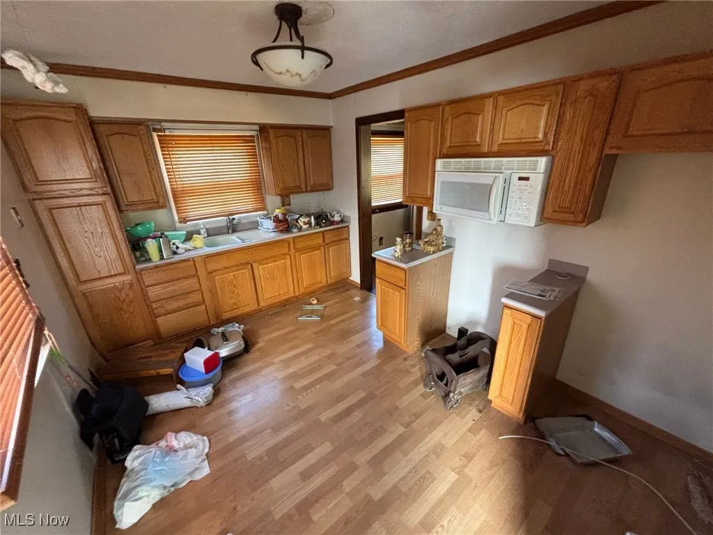 Kitchen featuring light countertops, ornamental molding, a sink, light wood-style floors, and white microwave