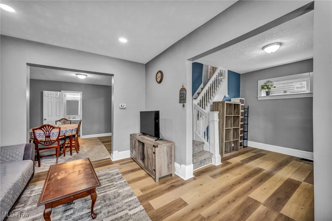 Living area featuring stairs, light wood-type flooring, baseboards, and a textured ceiling