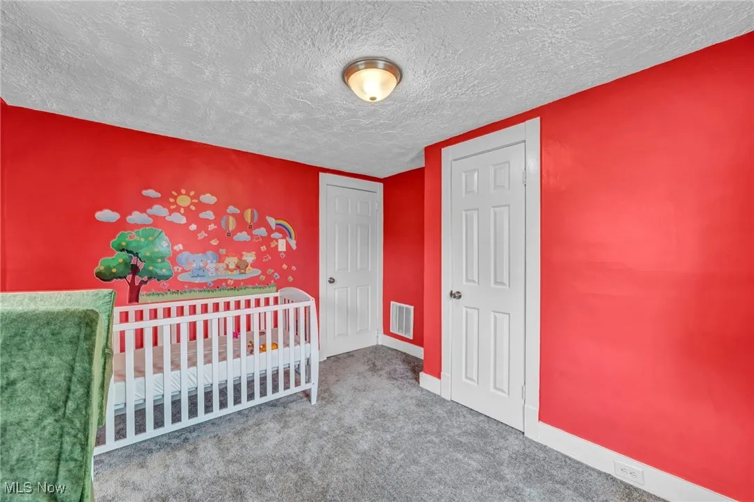 Unfurnished bedroom featuring carpet flooring, a nursery area, baseboards, a textured ceiling, and visible vents