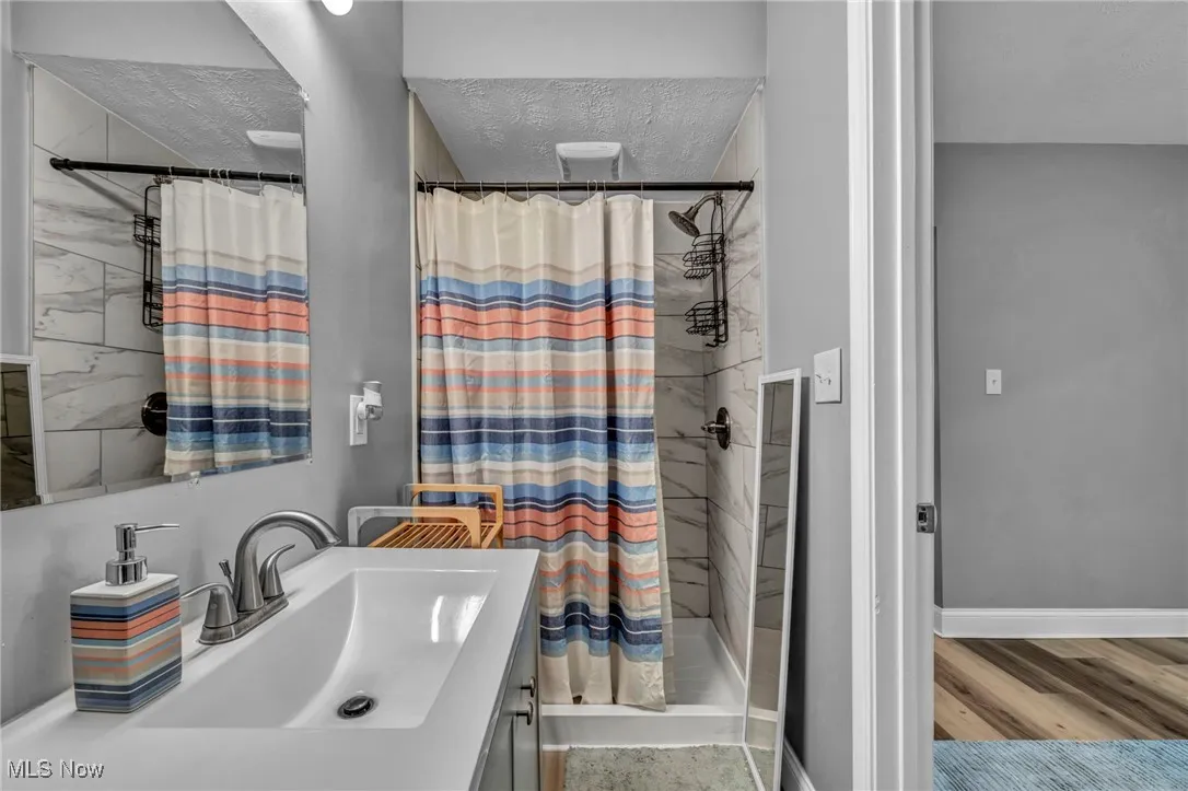 Bathroom featuring a textured ceiling, a shower stall, baseboards, wood finished floors, and vanity