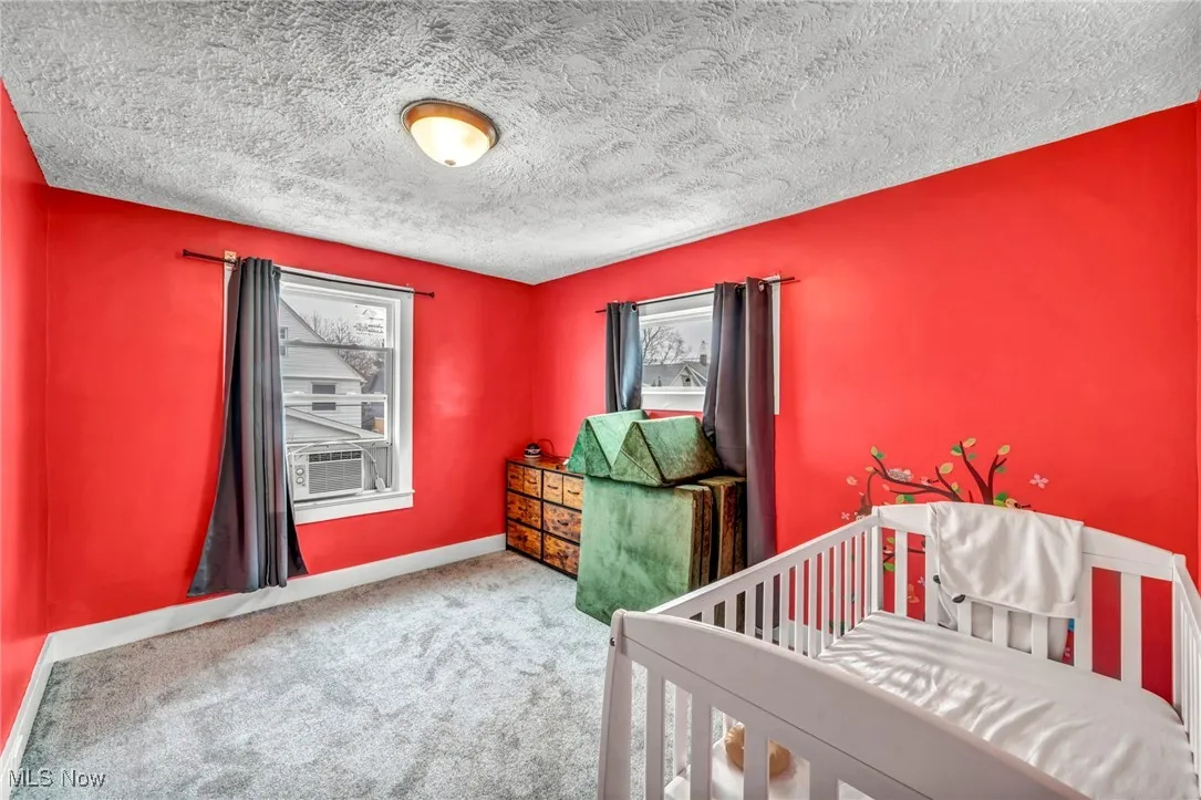 Bedroom featuring a textured ceiling, a crib, carpet, baseboards, and cooling unit