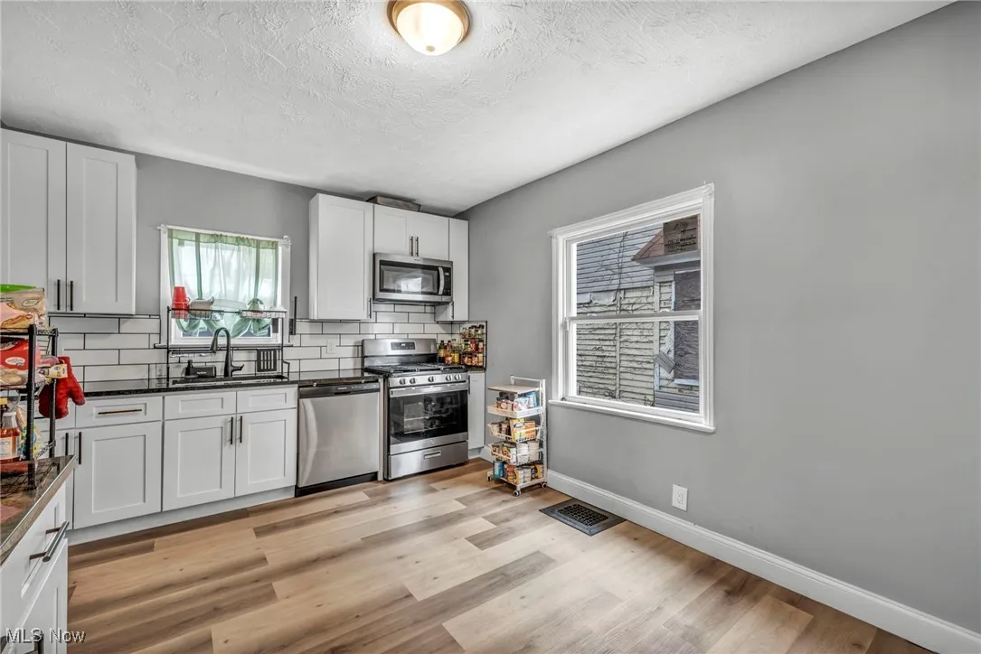Kitchen with a sink, appliances with stainless steel finishes, dark countertops, visible vents, and decorative backsplash