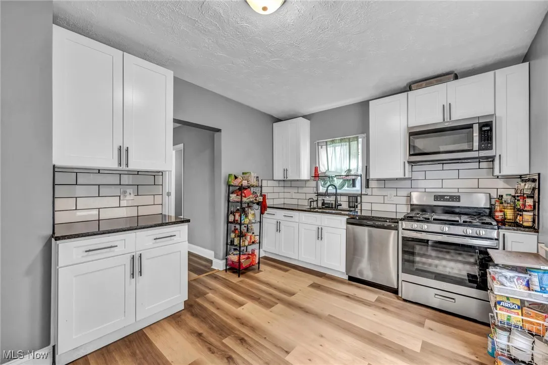 Kitchen with white cabinets, a sink, light wood-type flooring, and appliances with stainless steel finishes