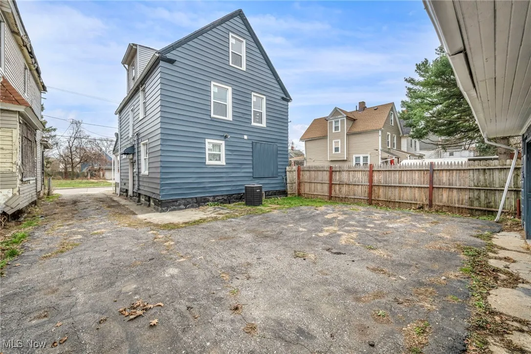 Back of property with central AC unit, driveway, and fence