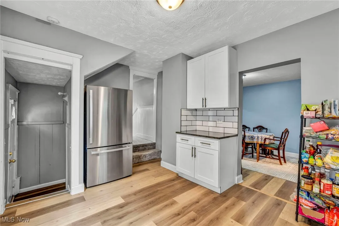 Kitchen with decorative backsplash, white cabinets, light wood-style flooring, dark countertops, and freestanding refrigerator