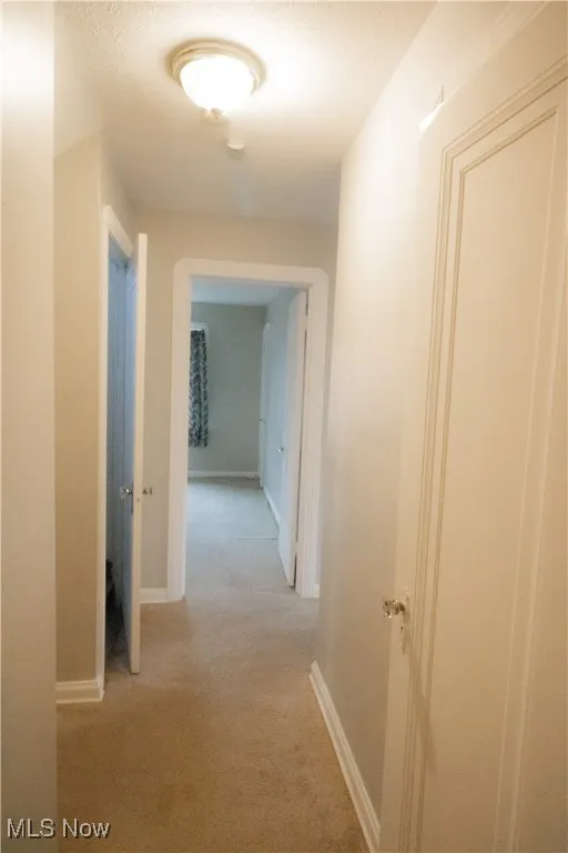 Upstairs hallway with baseboards, a textured ceiling, and light carpet