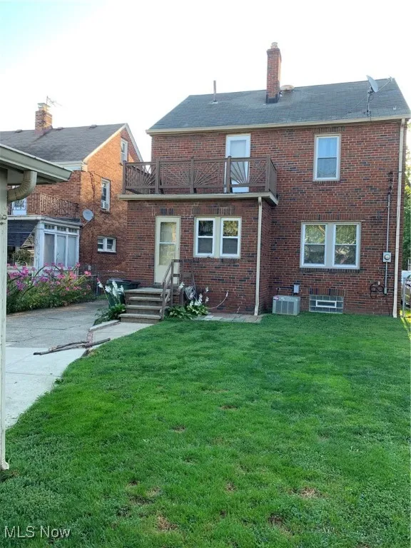 Rear view of property featuring a balcony, a lawn, a chimney, and brick siding