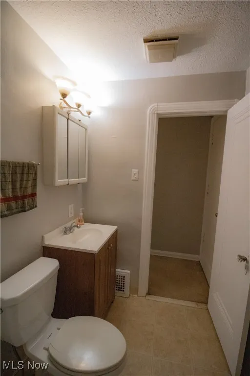Half bath with visible vents, toilet, vanity, and a textured ceiling