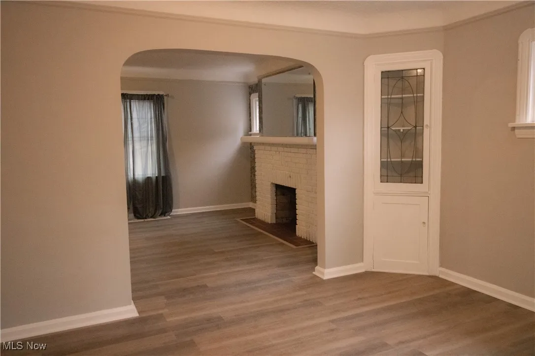 Unfurnished living room with arched walkways, baseboards, a fireplace, and wood finished floors