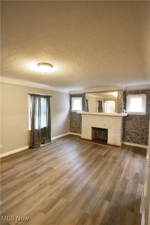 Unfurnished living room featuring baseboards, a textured ceiling, wood finished floors, and a brick fireplace