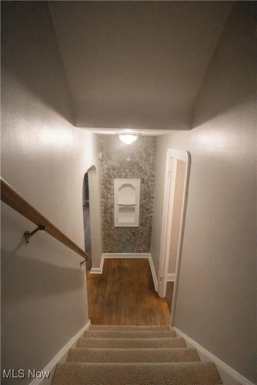 Stairway featuring baseboards, arched walkways, and wood finished floors